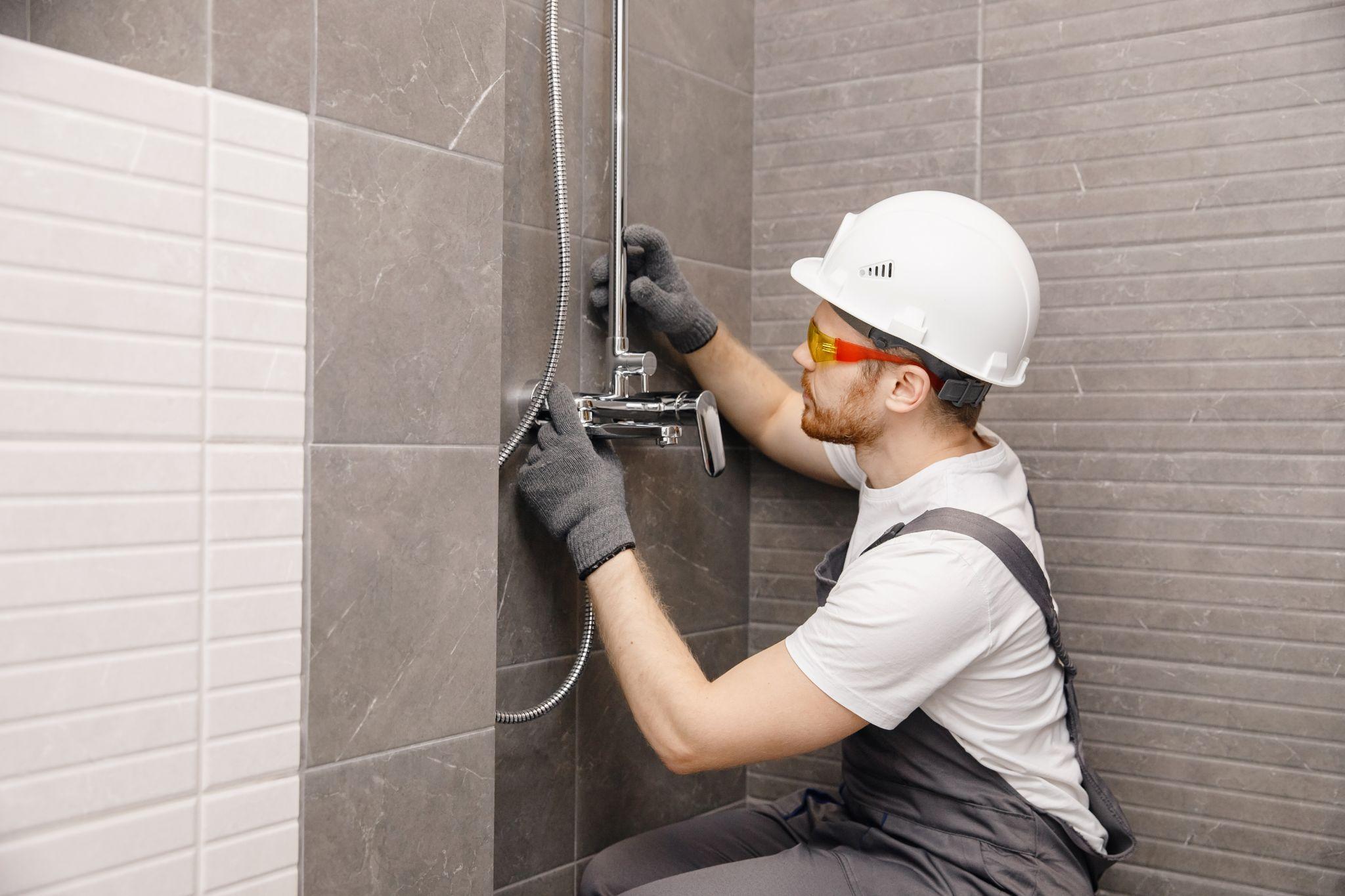 Plumber installing water taps shower stall, work in bathroom