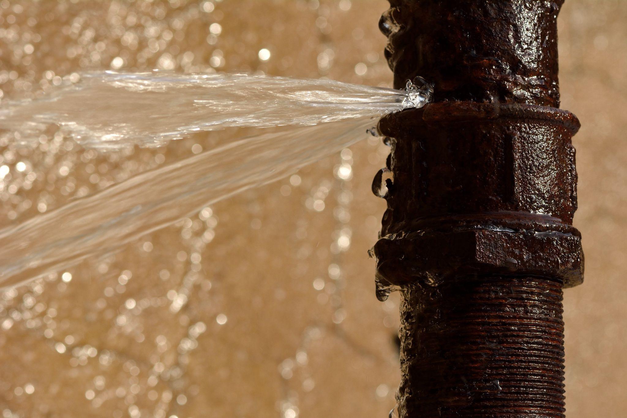 Rusty burst pipe squirting water at high pressure