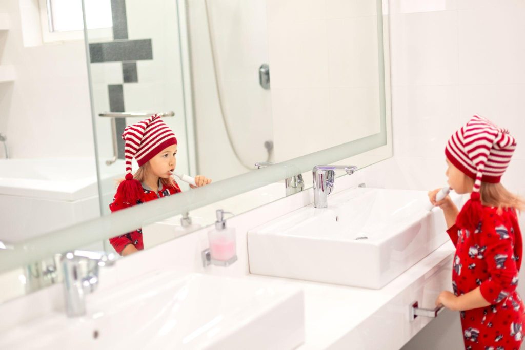 A little girl in Christmas pajamas brushing her teeth in the bathroom