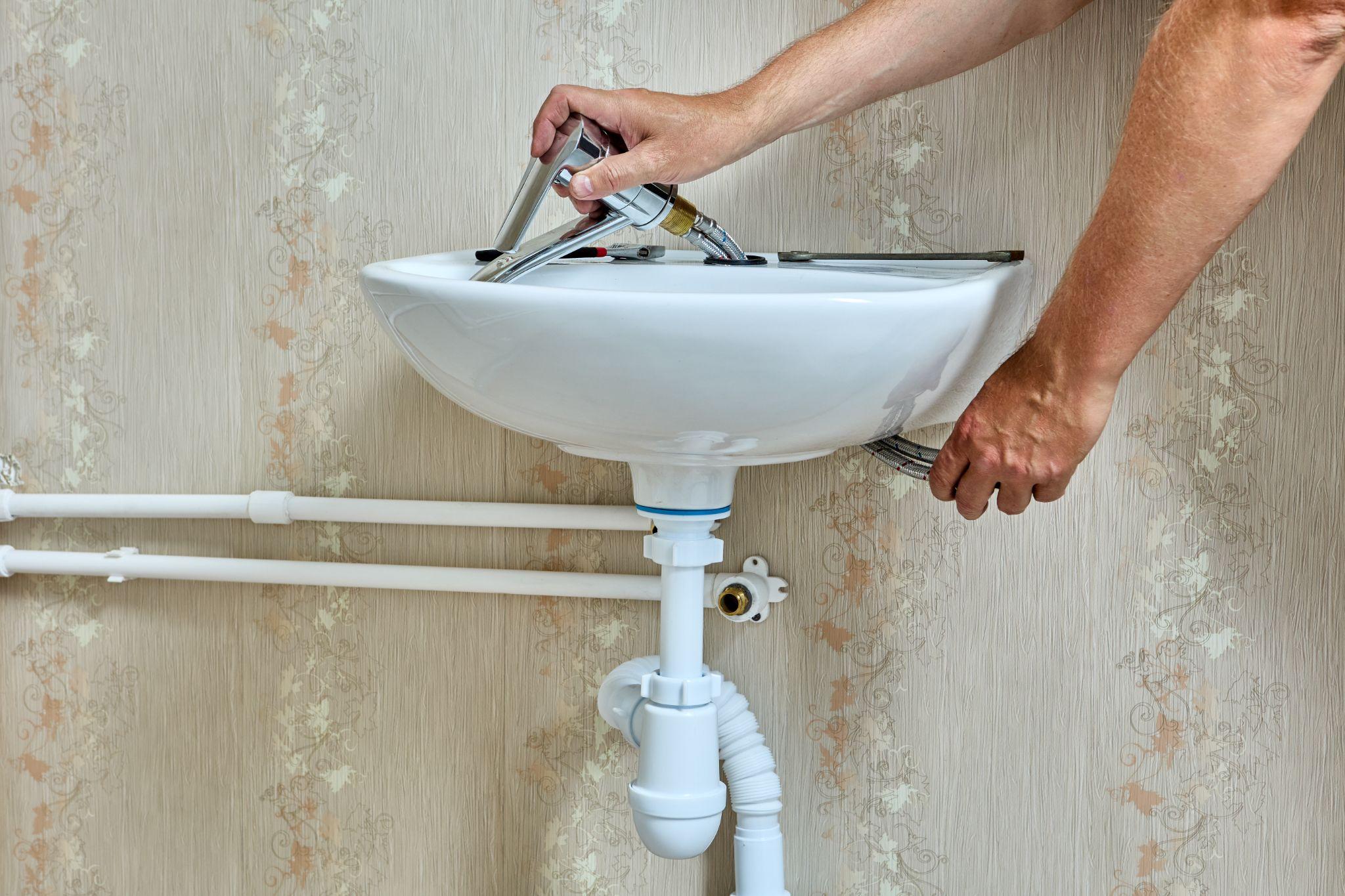 plumber installs faucet on sink in bathroom.