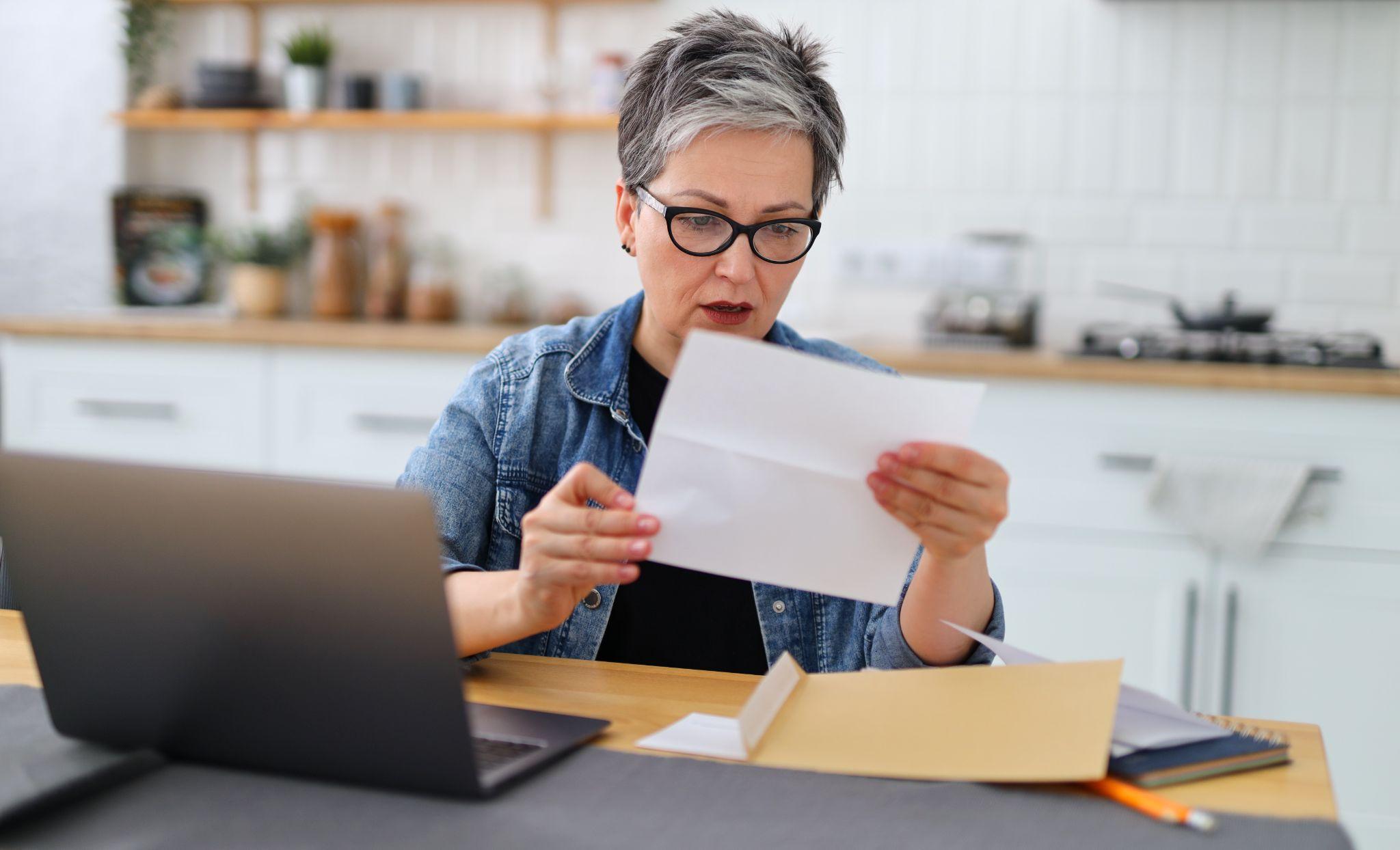 Shocked woman holding letter in home interior, high water bill for payment.