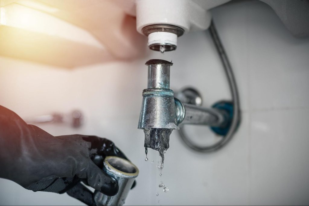 Leaking sink drain pipe connection being repaired, with water dripping from a disconnected joint