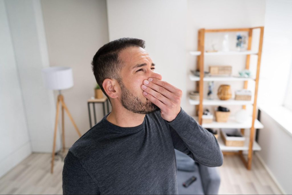 A man holding his nose in his house as if he smells something bad